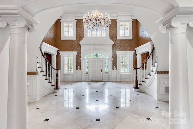 entrance foyer with ornate columns, a chandelier, ornamental molding, and a high ceiling