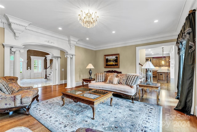 living room with an inviting chandelier, crown molding, light hardwood / wood-style floors, and decorative columns