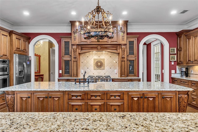 kitchen featuring a center island with sink, stainless steel appliances, backsplash, hanging light fixtures, and light stone countertops