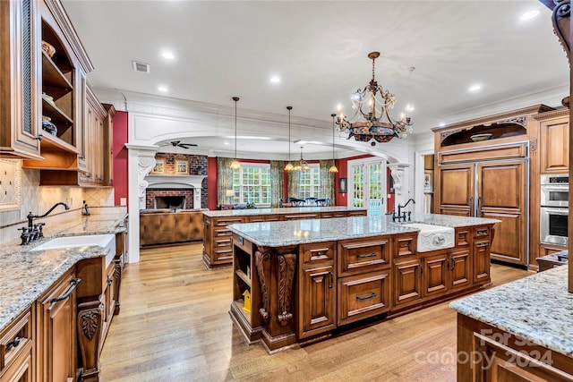 kitchen featuring pendant lighting, a center island with sink, light hardwood / wood-style flooring, light stone countertops, and ornamental molding