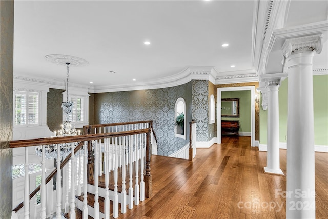 corridor with ornate columns, crown molding, hardwood / wood-style flooring, and an inviting chandelier