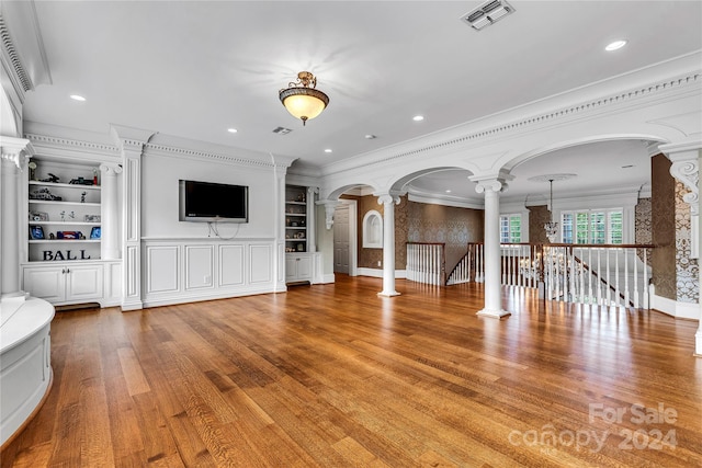 unfurnished living room featuring built in shelves, wood-type flooring, crown molding, and ornate columns