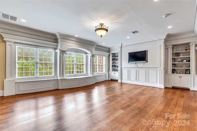 unfurnished living room featuring crown molding, built in features, and hardwood / wood-style floors