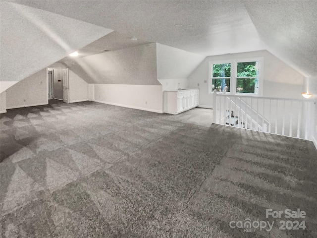 additional living space featuring vaulted ceiling, sink, a textured ceiling, and dark colored carpet