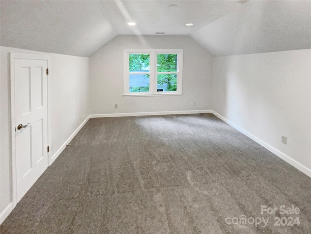 additional living space with a textured ceiling, lofted ceiling, and dark colored carpet
