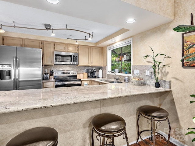 kitchen with sink, a breakfast bar, light stone counters, and appliances with stainless steel finishes