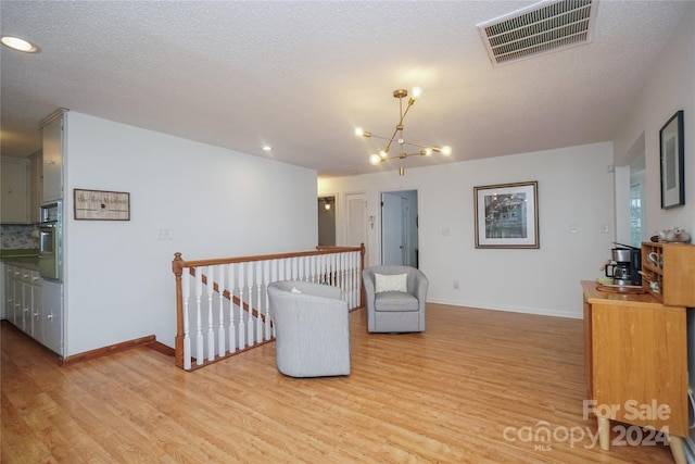 living area with a textured ceiling, light hardwood / wood-style flooring, and a notable chandelier