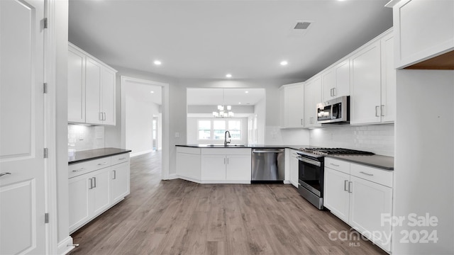 kitchen with backsplash, white cabinets, sink, light wood-type flooring, and appliances with stainless steel finishes