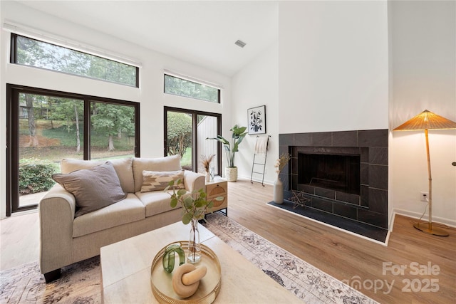 living room with hardwood / wood-style flooring, a towering ceiling, and a tile fireplace