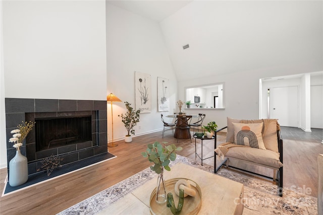 living room with hardwood / wood-style flooring, high vaulted ceiling, and a tiled fireplace