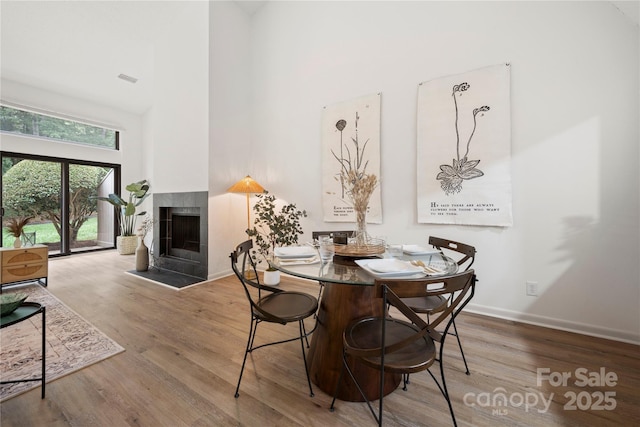 dining room featuring wood-type flooring, a towering ceiling, and a tiled fireplace