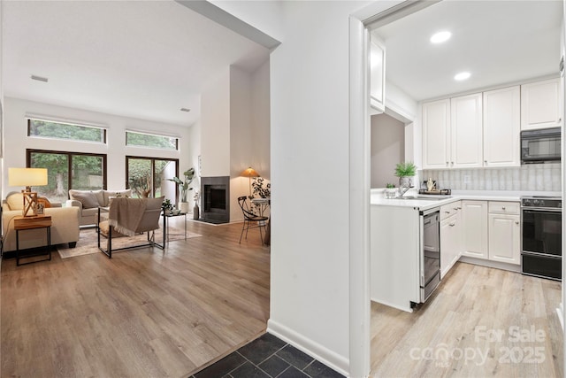 kitchen featuring decorative backsplash, white cabinetry, light hardwood / wood-style flooring, and black appliances