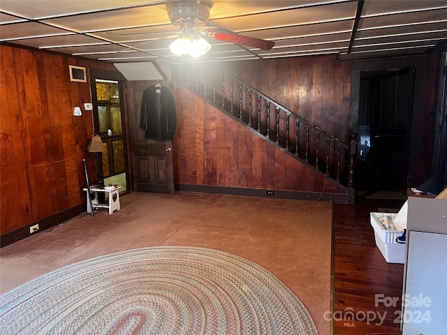 basement with ceiling fan and wooden walls