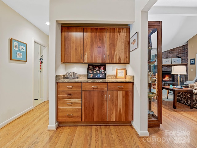 kitchen featuring light hardwood / wood-style floors, brick wall, and stone counters