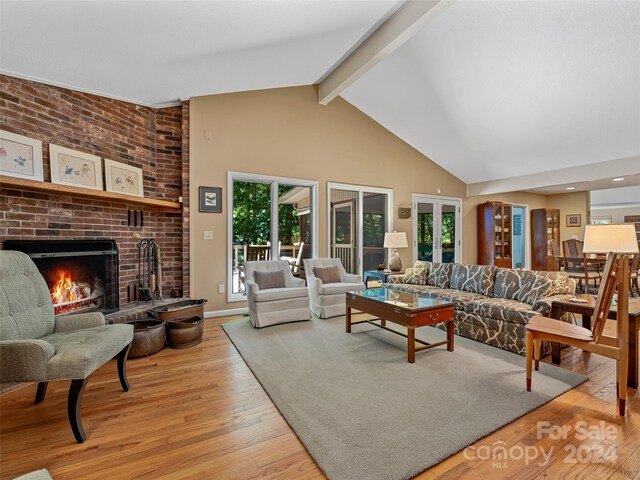 living room featuring beam ceiling, a brick fireplace, light hardwood / wood-style flooring, and a wealth of natural light