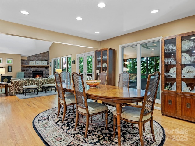 dining area featuring a brick fireplace, vaulted ceiling, and light hardwood / wood-style flooring