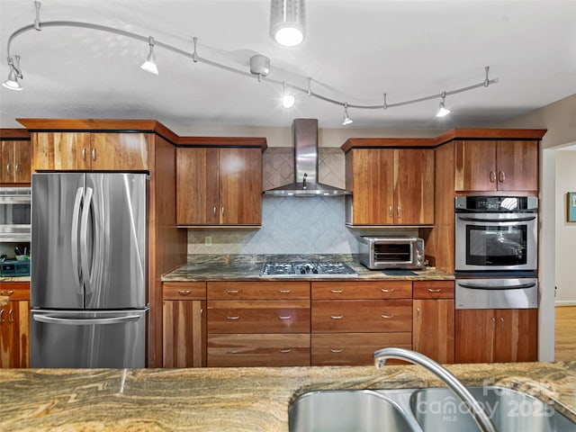 kitchen with sink, stainless steel appliances, tasteful backsplash, light stone countertops, and wall chimney exhaust hood