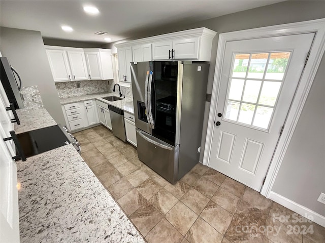 kitchen with appliances with stainless steel finishes, tasteful backsplash, light stone counters, sink, and white cabinets