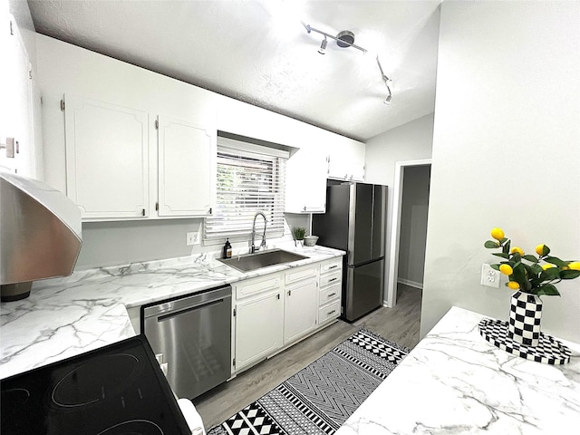 kitchen with appliances with stainless steel finishes, white cabinets, vaulted ceiling, light hardwood / wood-style flooring, and sink