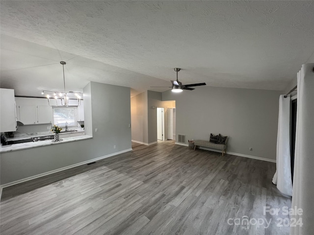 unfurnished living room featuring a textured ceiling, vaulted ceiling, ceiling fan with notable chandelier, light hardwood / wood-style flooring, and sink