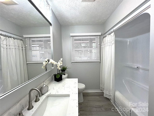 full bathroom with a textured ceiling, wood-type flooring, vanity, toilet, and shower / bath combo