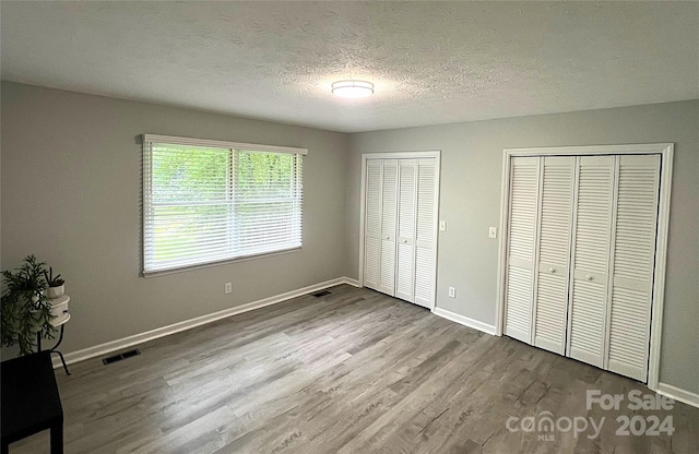 unfurnished bedroom with a textured ceiling, multiple closets, and hardwood / wood-style floors