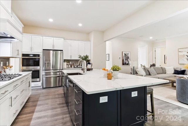 kitchen with white cabinets, stainless steel appliances, an island with sink, decorative backsplash, and custom range hood