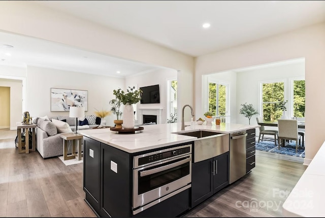 kitchen with hardwood / wood-style floors, an island with sink, stainless steel appliances, light stone counters, and sink