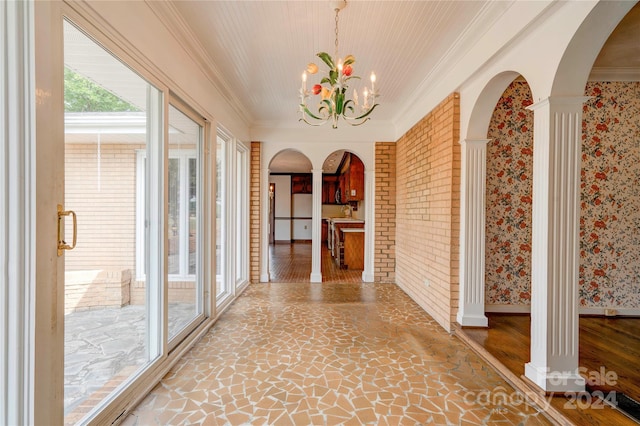 corridor featuring ornate columns, crown molding, and a notable chandelier