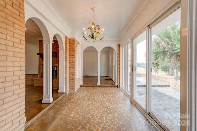 interior space with a chandelier, decorative columns, and brick wall