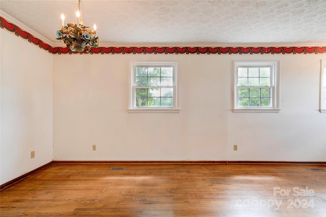 empty room featuring light hardwood / wood-style floors, crown molding, a textured ceiling, and an inviting chandelier