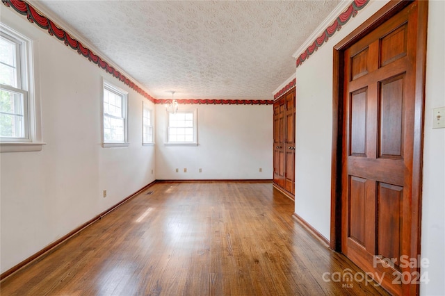 unfurnished room with hardwood / wood-style floors, a textured ceiling, ornamental molding, and a notable chandelier