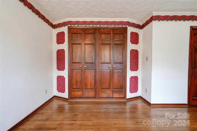 unfurnished bedroom featuring crown molding, a closet, a textured ceiling, and hardwood / wood-style flooring