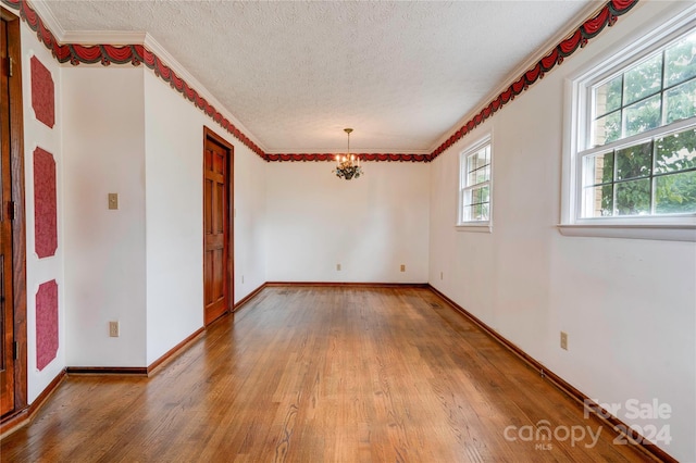 spare room with hardwood / wood-style floors, a textured ceiling, an inviting chandelier, and ornamental molding