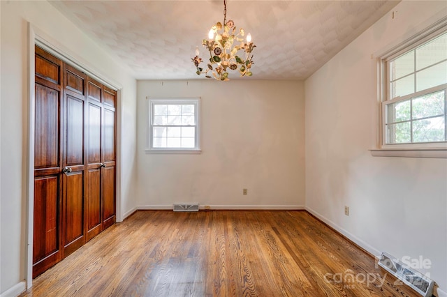 unfurnished dining area with a textured ceiling, light hardwood / wood-style flooring, and a notable chandelier