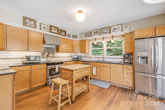 kitchen featuring extractor fan, dark stone counters, light wood-type flooring, sink, and stainless steel appliances