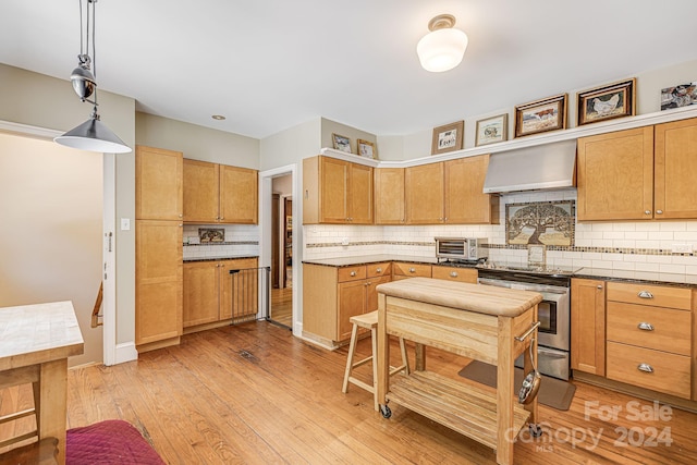 kitchen featuring decorative backsplash, hanging light fixtures, ventilation hood, stainless steel range oven, and light hardwood / wood-style floors