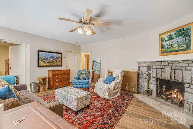 living room with a stone fireplace, light hardwood / wood-style floors, and ceiling fan