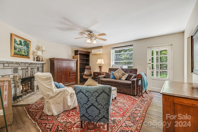 living room with ceiling fan, hardwood / wood-style flooring, a wall mounted AC, and a stone fireplace