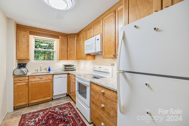 kitchen with white appliances, light stone counters, and sink