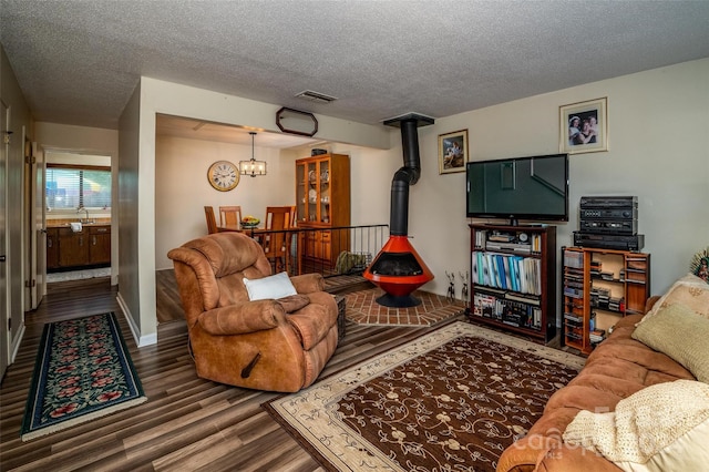 living room with hardwood / wood-style floors, a wood stove, sink, a textured ceiling, and a chandelier