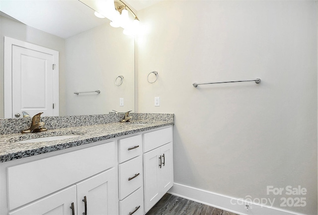 bathroom with double vanity, baseboards, wood finished floors, and a sink