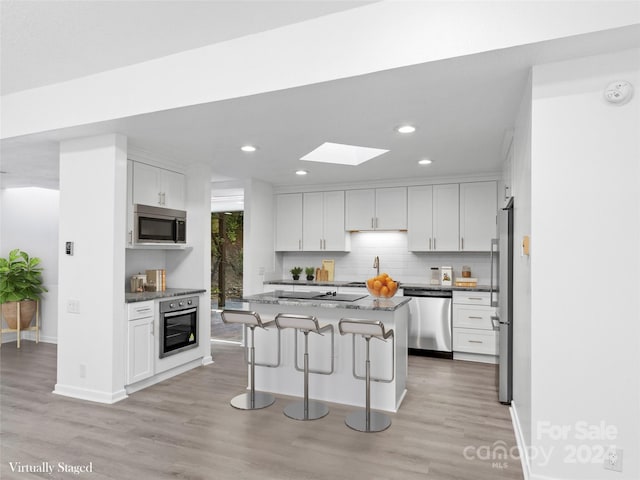 kitchen featuring light stone countertops, appliances with stainless steel finishes, white cabinetry, and a center island