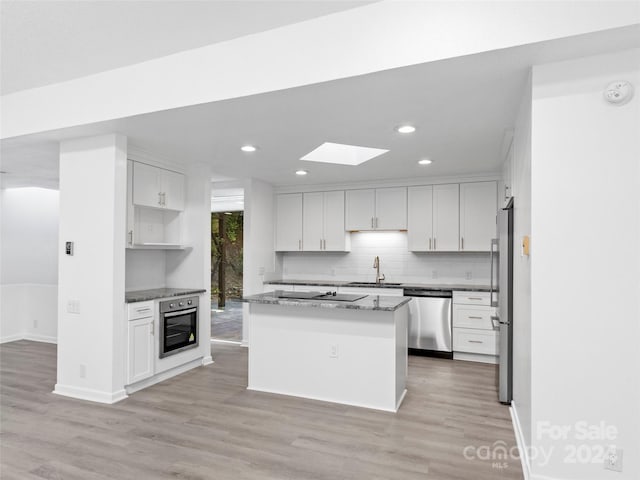 kitchen with appliances with stainless steel finishes, dark stone countertops, a kitchen island, white cabinets, and sink