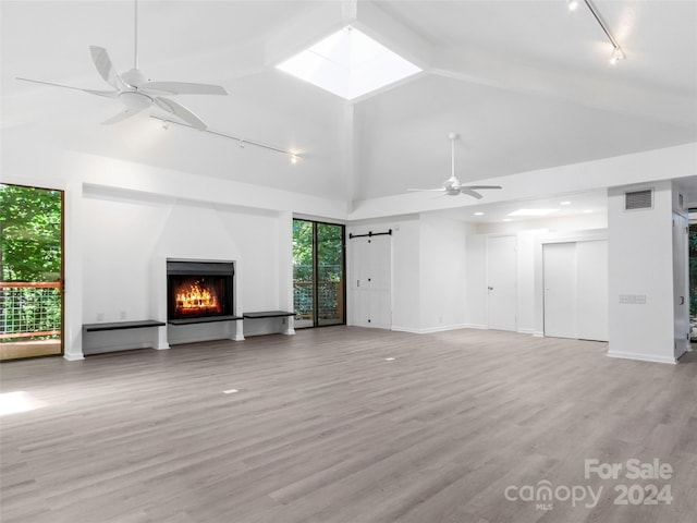 unfurnished living room featuring ceiling fan, a barn door, vaulted ceiling with skylight, light hardwood / wood-style floors, and rail lighting