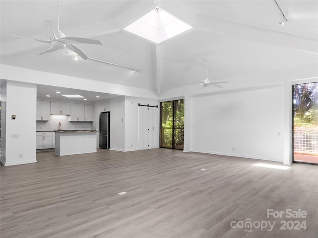 unfurnished living room featuring a skylight, sink, ceiling fan, light hardwood / wood-style flooring, and a barn door