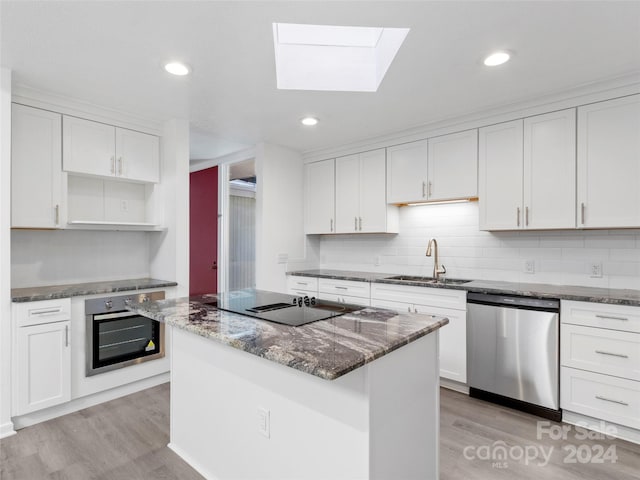 kitchen featuring appliances with stainless steel finishes, a center island, white cabinetry, sink, and light hardwood / wood-style flooring