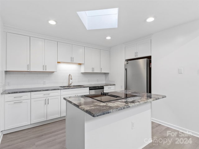 kitchen with white cabinets, a kitchen island, stainless steel appliances, dark stone counters, and sink