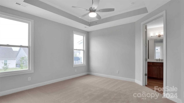 unfurnished bedroom featuring light carpet, a tray ceiling, ensuite bath, and ceiling fan