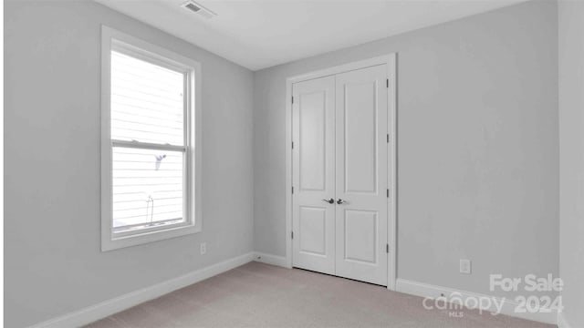 unfurnished bedroom featuring a closet, light carpet, and multiple windows